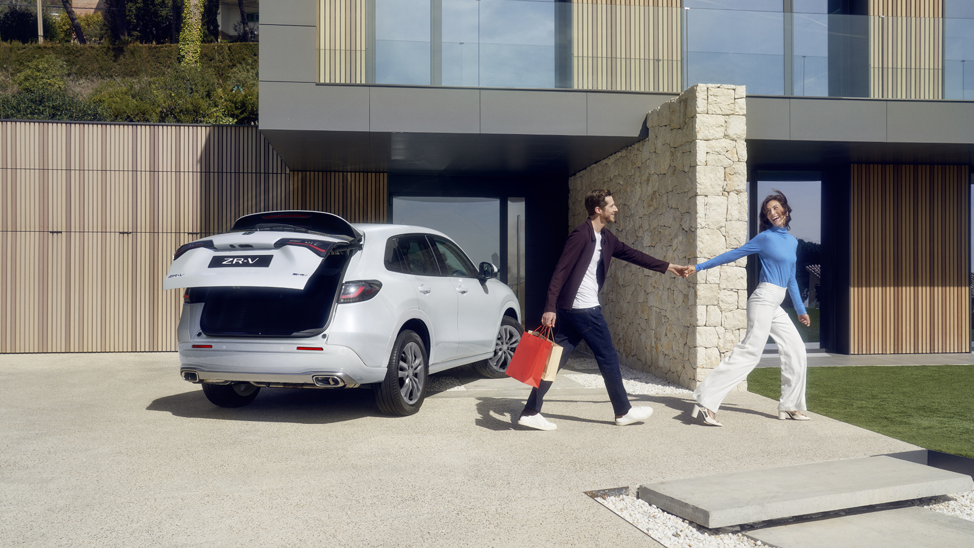 Bílý vůz ZR-V na příjezdové cestě s elektricky ovládanými dveřmi zavazadlového prostoru