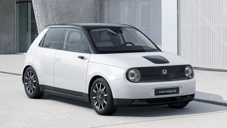 Přední tříčtvrteční pohled na zaparkovaný vůz Honda e s budovou v pozadí