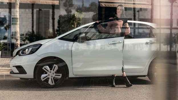 Boční pohled na zaparkovaný model Honda Jazz a na ženu otevírající dveře