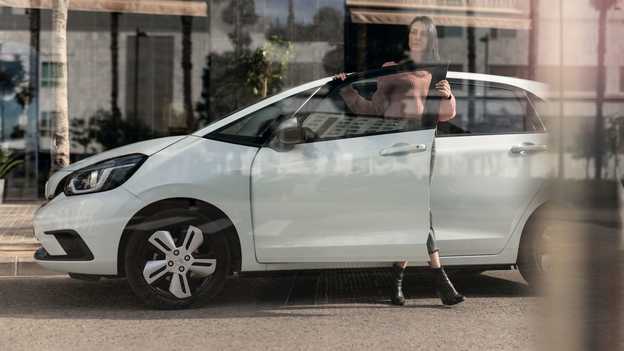 Boční pohled na zaparkovaný model Honda Jazz a na ženu otevírající dveře