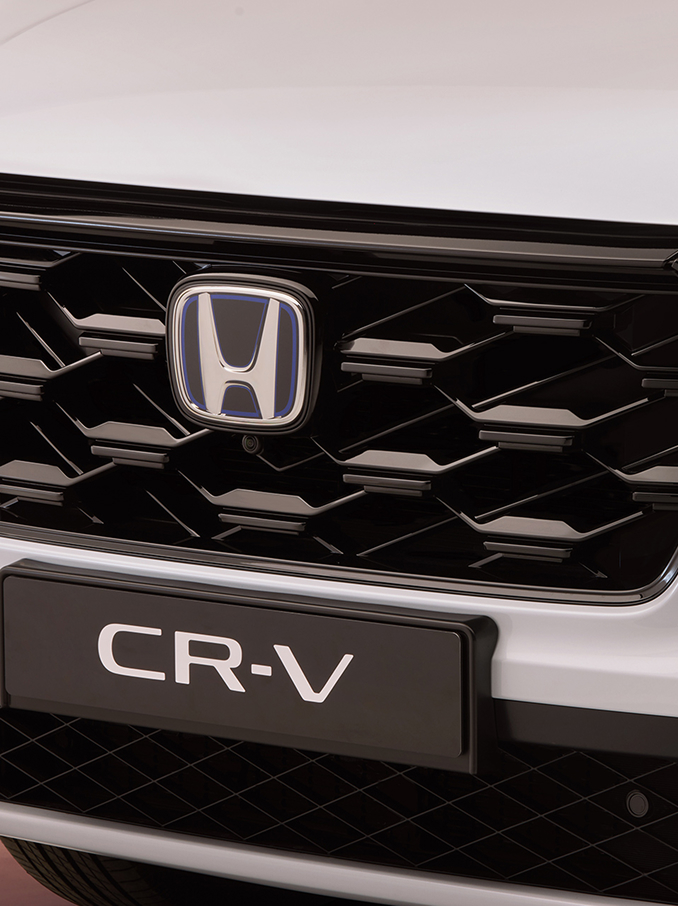 Detailní záběr masky chladiče modelu Honda CR-V s černým voštinovým vzorem, logem Honda uprostřed a názvem modelu CR-V viditelným pod ním.