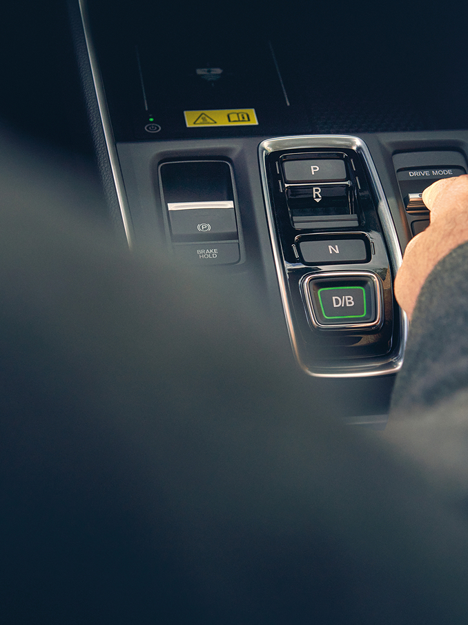 Ruka osoby, která se natahuje, aby nastavila přepínač na středové konzole moderního automobilu vedle tlačítek voliče převodovky.