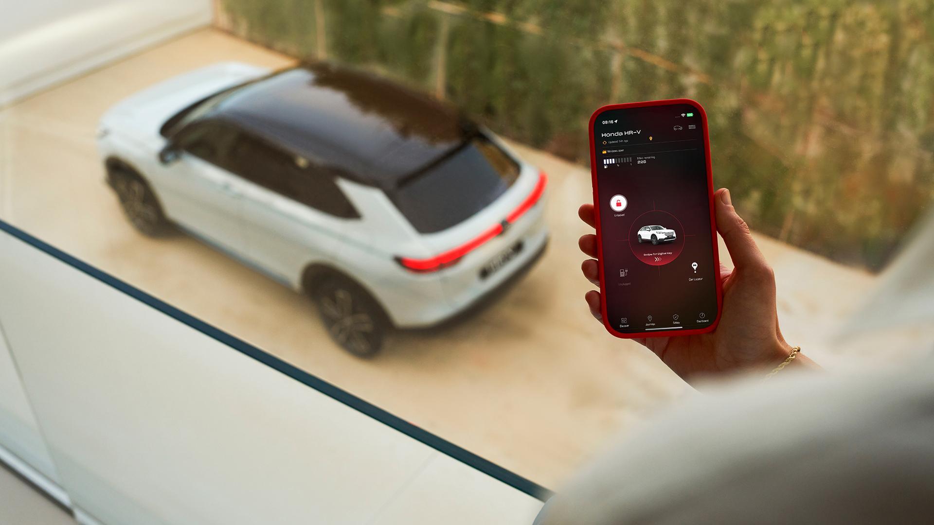 Osoba drží chytrý telefon zobrazující aplikaci pro nastavení nabíjení vozidla, zatímco v pozadí je zaparkované bílé SUV.