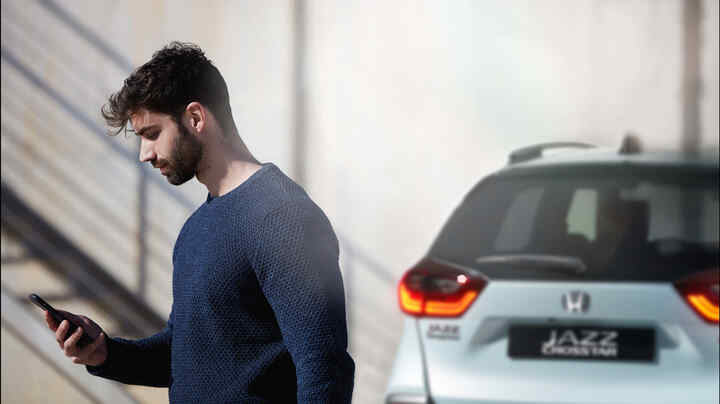 Osoba, která se dívá na smartphone, a v pozadí stojí Honda Jazz Crosstar.