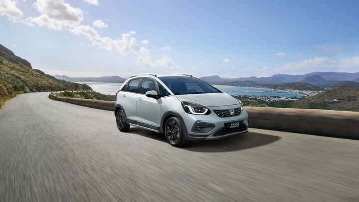 Jízda s vozem Honda Jazz Hybrid zepředu ve 3/4 s výhledem na krajinu v pozadí.