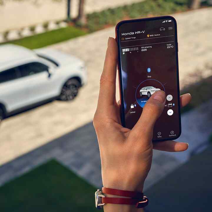 Detailní záběr na dámu používající digitální klíč. V dálce je vidět vůz Honda HR-V.