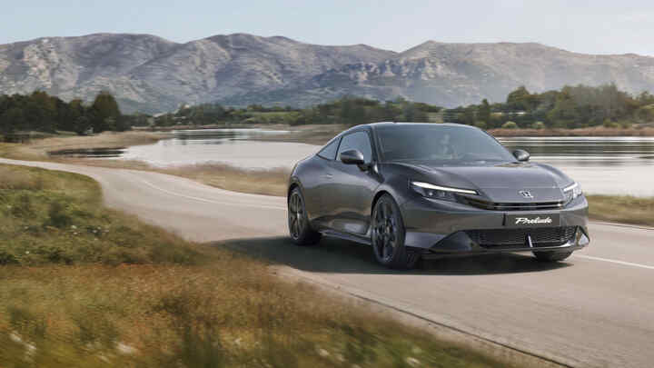 Boční profil vozu Honda Prelude Hybrid projíždějícího vedle jezera se svěžími zelenými stromy.