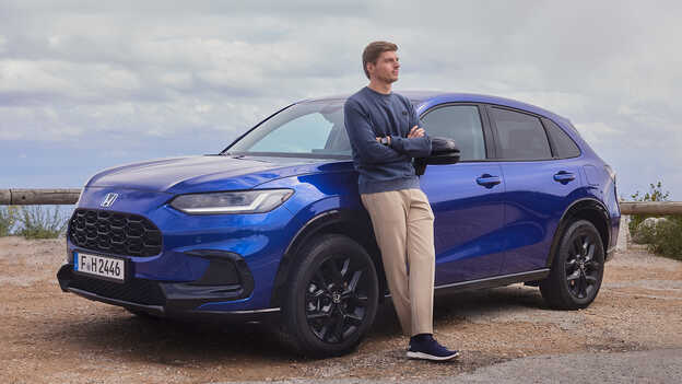 Max Verstappen u stojícího modrého hybridního SUV Honda ZR-V se sportovním vzhledem.