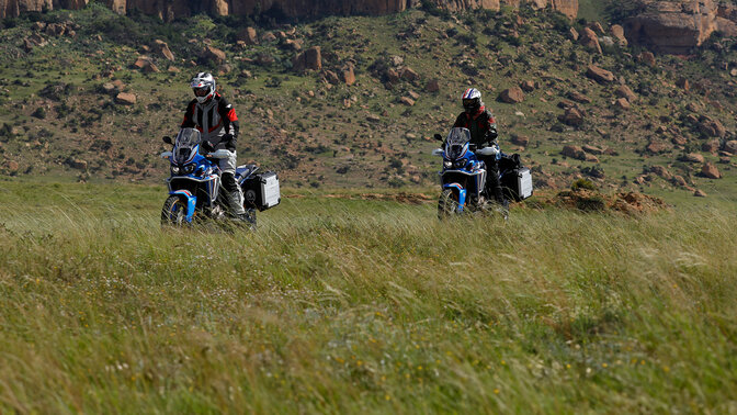 Dva jezdci HAR v terénu s horami v pozadí