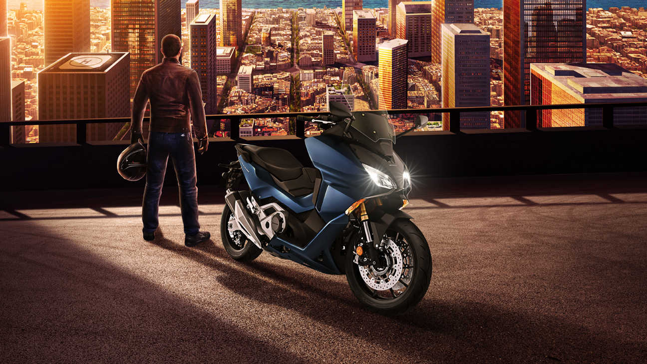 Honda Forza 750, pravý přední poloprofil, muž stojící vedle zaparkovaného motocyklu nad městem, modrý motocykl