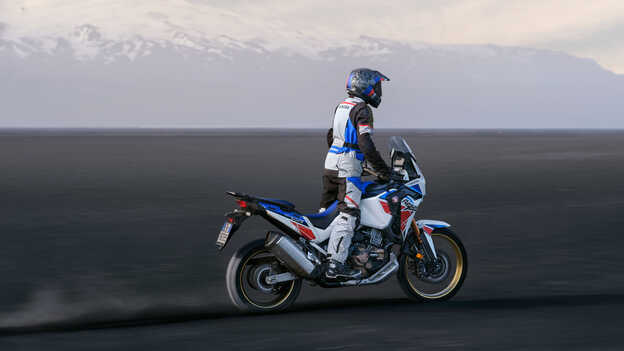 Zadní tříčtvrtinový pohled na motocykl Honda Africa Twin projíždějící dunami.
