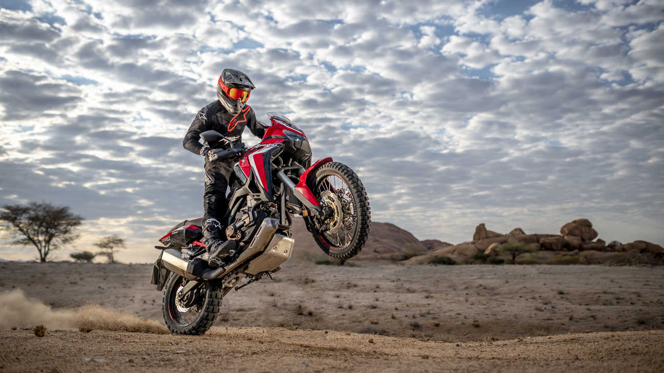 Honda Africa Twin, přední pravý poloprofil, jízda na zadním kole pouštní krajinou