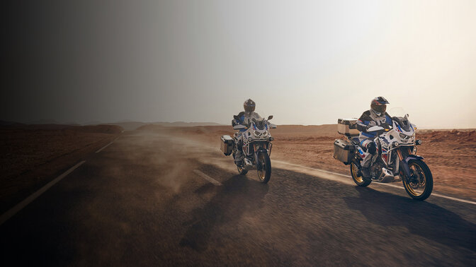 Přední tříčtvrtinový pohled na jezdce na strojích CRF1100 Africa Twin Adventure Sports na silnici v poušti 