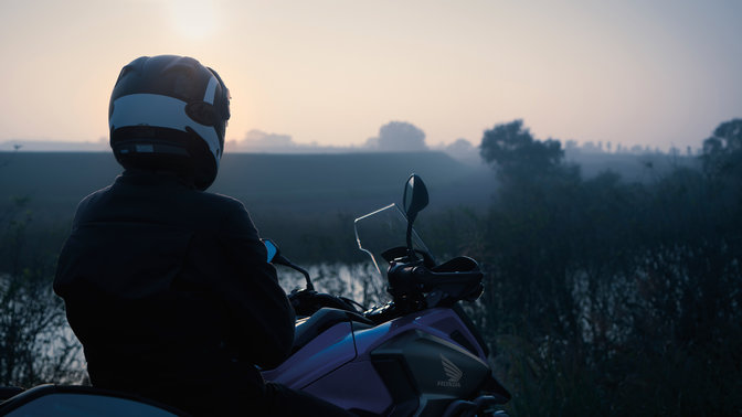 Jezdec sedící na modelu Honda NC750X zaparkovaném ve venkovské oblasti