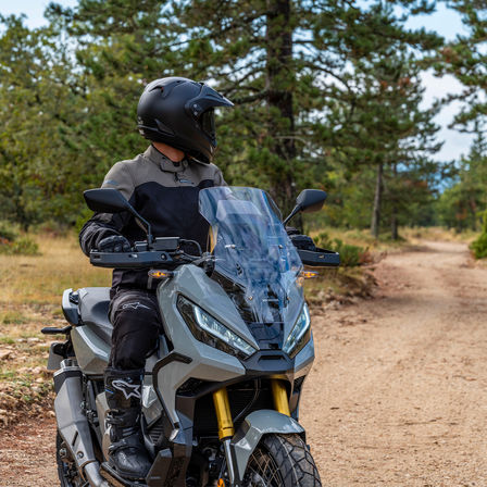 Honda X-ADV, přední pravý poloprofil, jezdec stojící na šedém motocyklu, na lesní cestě