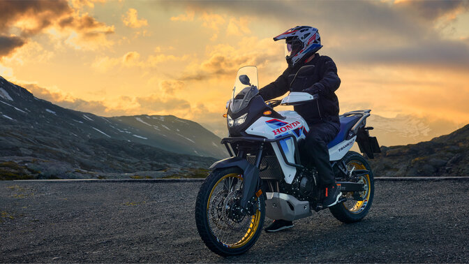 Model na motocyklu XL750 Transalp na silnici v horské lokalitě.