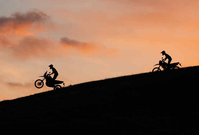 Dva motocykly Honda řady 300 jedoucí z kopce při západu slunce