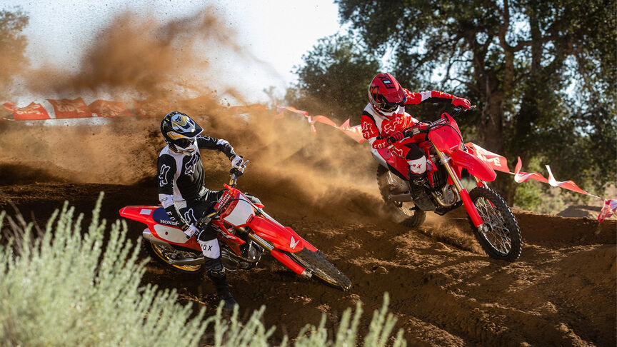 Dva jezdci překonávají skokánky na modelu Honda CRF450R.