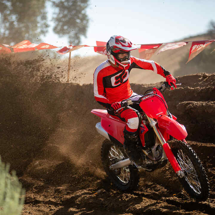 Model Honda CRF450R při jízdě v terénu s horami v pozadí.