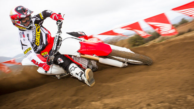 Front 3-quarter view of CRF250R leaning into corner with rider. Dirt track location.