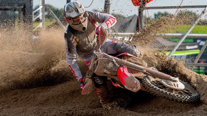 Přední tříčtvrtinový pohled na terénní motocykl Honda s jezdcem projíždějícím smykem rozbahněný terén
