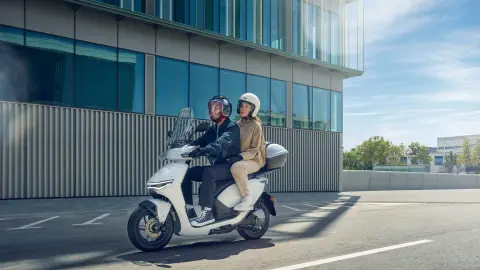 Figuranti jedoucí na skútru Honda CUV e: ve městě