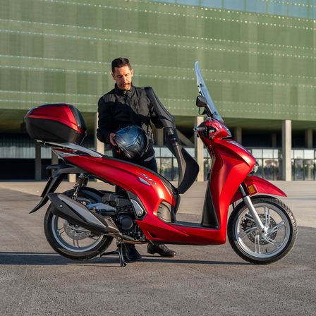 Honda SH350i, muž stojící vedle skútru, pohled zezadu, červený motocykl