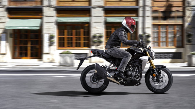 Boční pohled na model Honda CB300R Neo Sports Café jedoucí po silnici.
