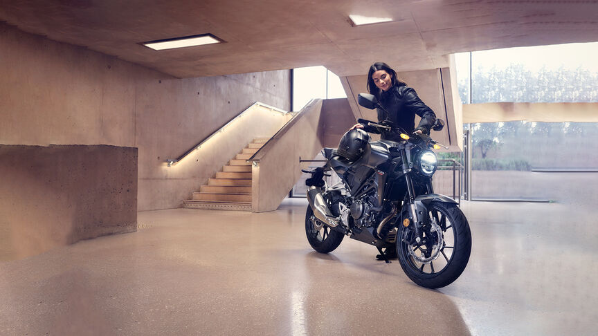 Tříčtvrtinový pohled zepředu na stroj Honda CB300R ve studiu, který si prohlíží žena.