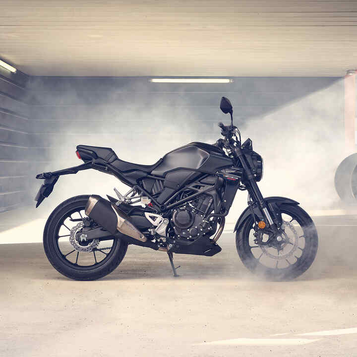 Boční pohled na motocykl Honda CB300R zaparkovaný v zaprášené garáži.
