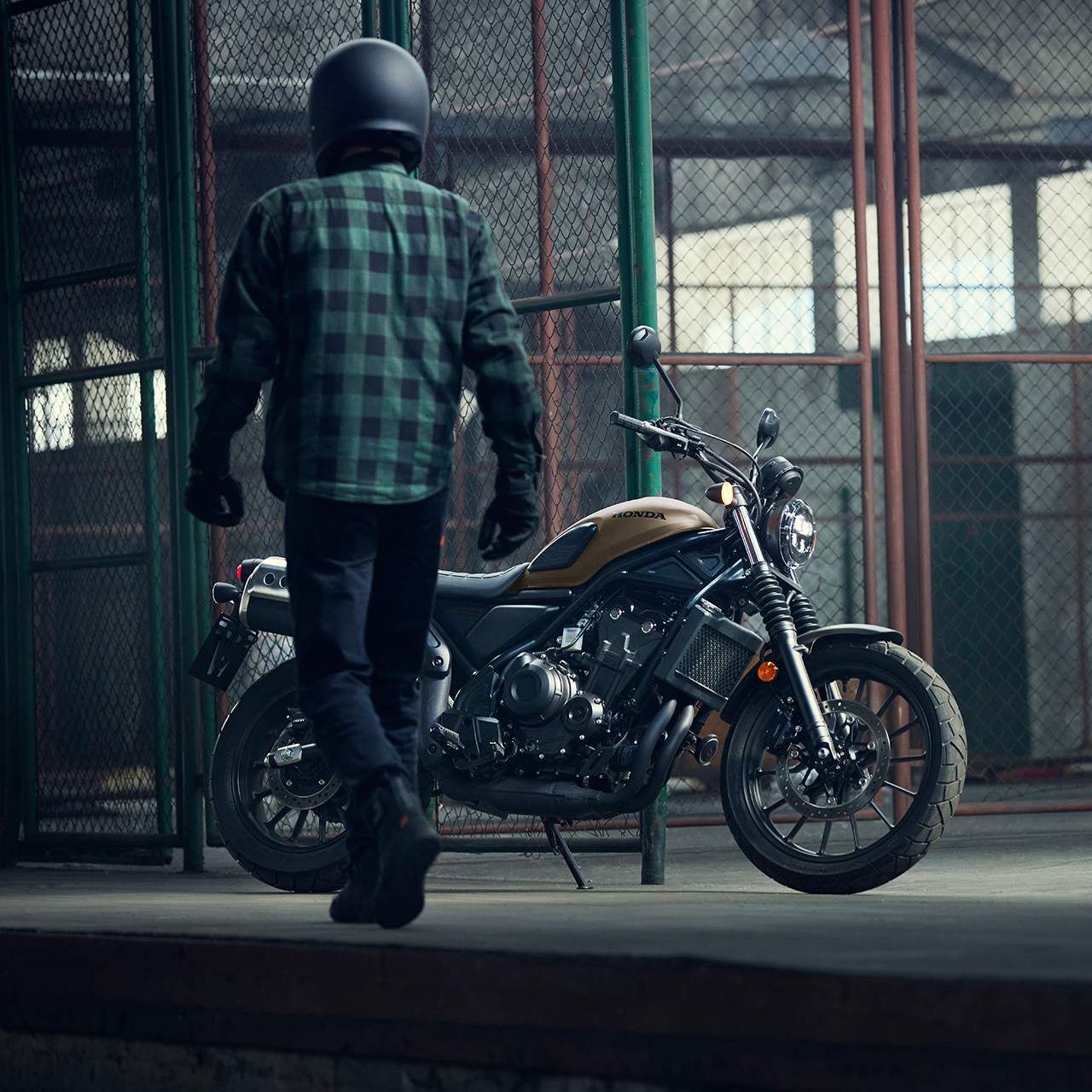 Jezdec prochází kolem zaparkovaného motocyklu Honda CL500 v prostorách skladu.
