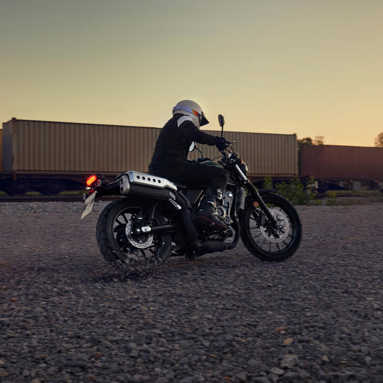 Figurant jedoucí na motocyklu Honda CL500 v prostorách skladu.