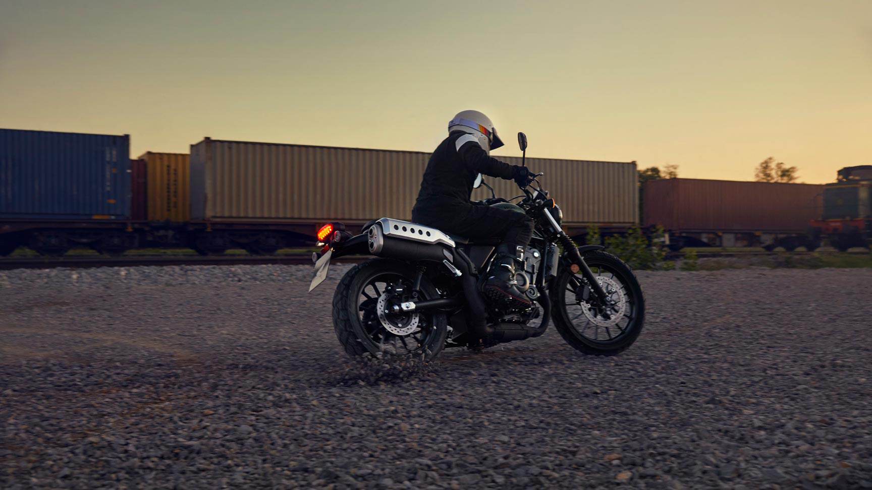 Figurant jedoucí na motocyklu Honda CL500 v prostorách skladu.