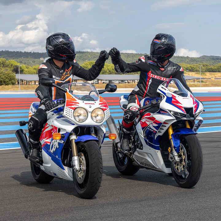 Záběr zepředu na dva jezdce sedící na motocyklech Honda Fireblades ťukající si pěstmi na závodní dráze.
